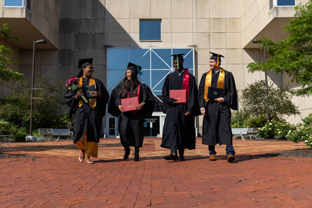 four students with diplomas wearing graduation cap and gown