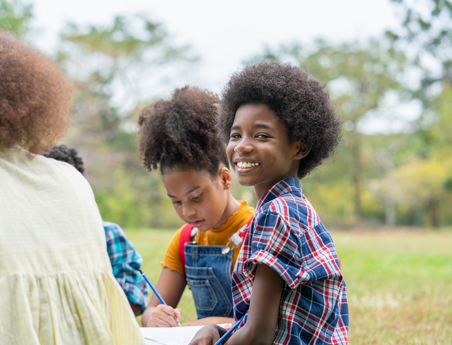 A group of Black schoolchildren smiling & studying together outside.