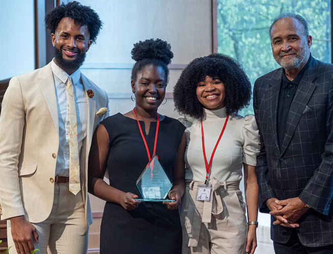 A female student holding a leadership award and posing with three other people.