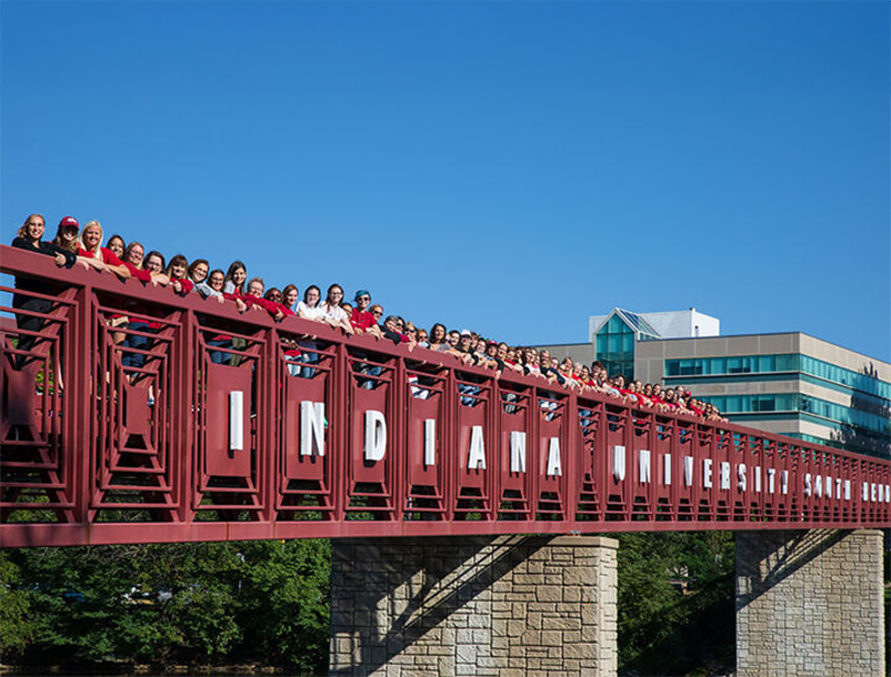 A group of women posing on a red Indiana University South Bend bridge.