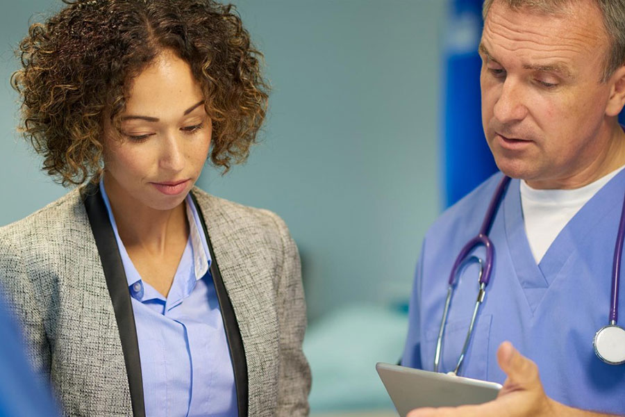 A doctor and administrator look down studying an ipad.