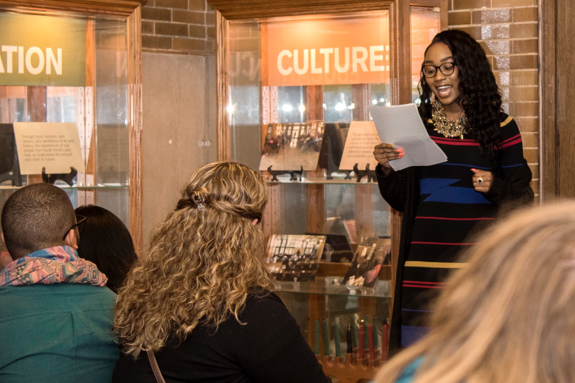 A Black woman reads in front of an audience at the Civil Rights Heritage Center.
