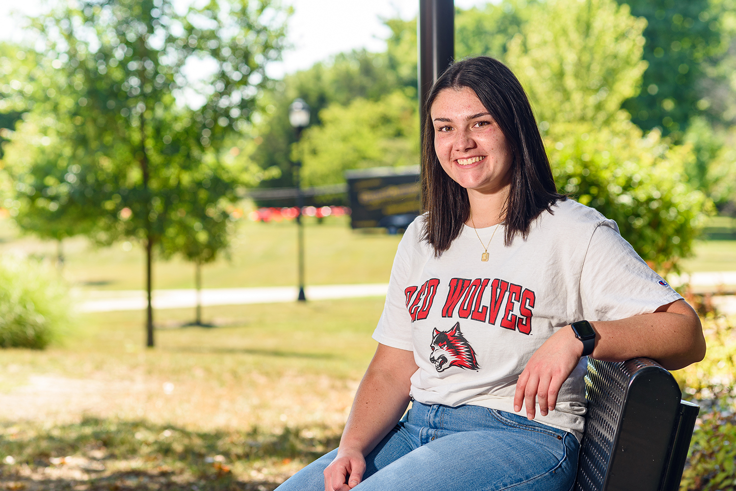 IU East student wearing a Red Wolves tee shirt seated on a bench on campus.