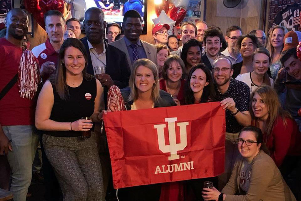 A big, diverse group of IU alumni with an IU flag gathered at a sports bar.