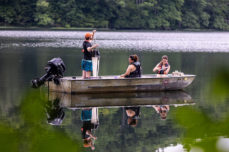 Three students conduct research in a boat on a lake.