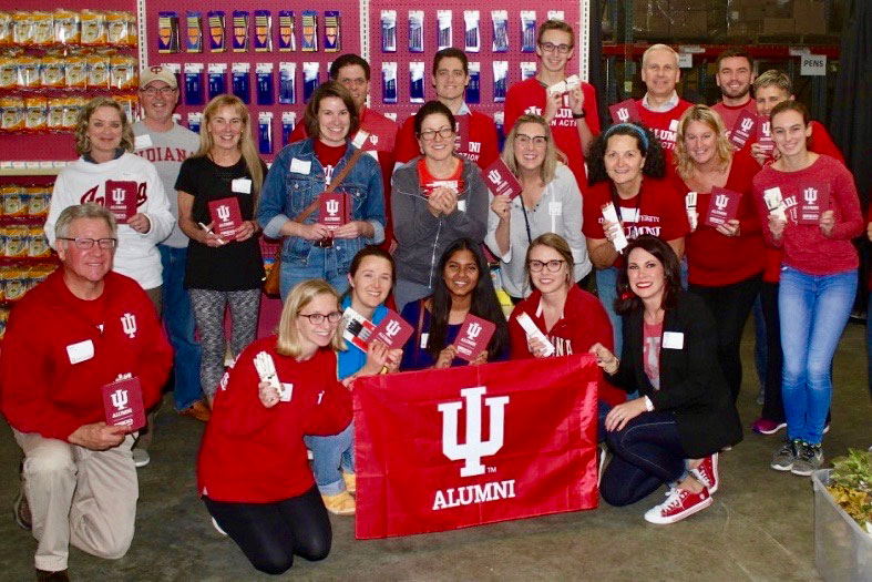 A diverse group of happy Indiana Unversity alumni holding an IU flag.