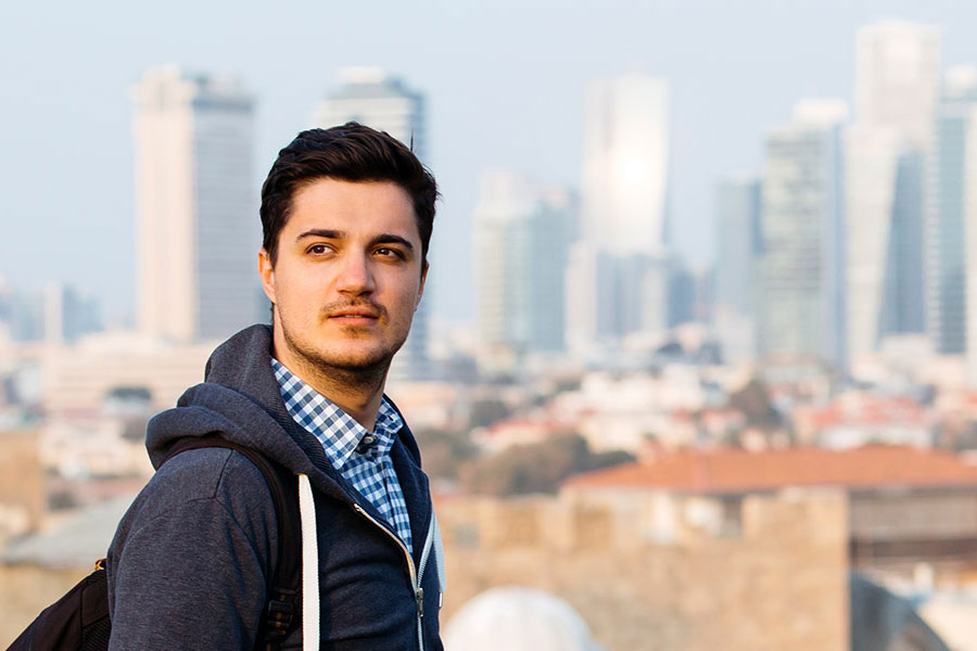 A male student stands in front of an Israeli skyline.