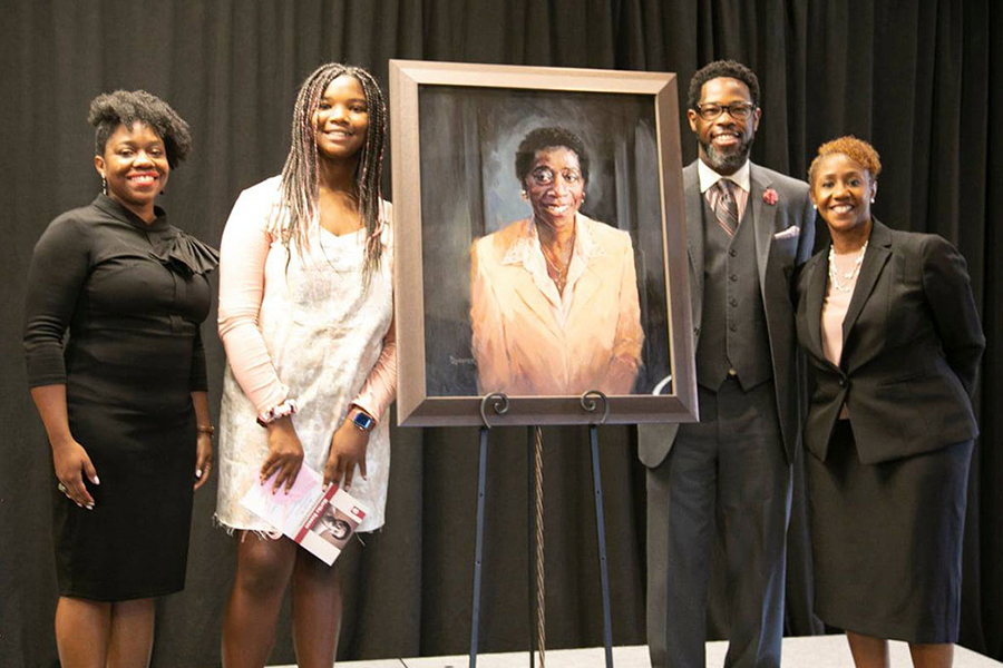 Four smiling people stand next to an oil painting of Martha Dawson.