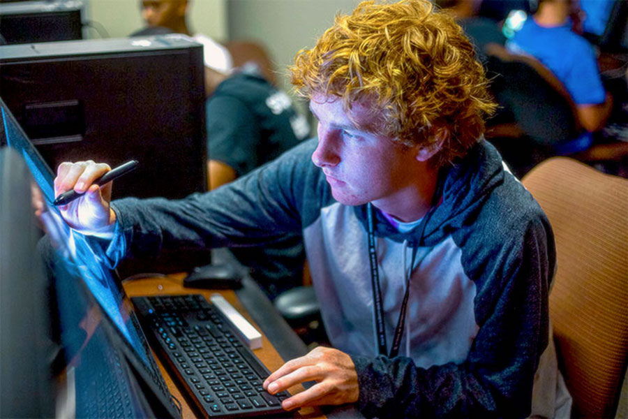 A male student draws with a stylus pen on a computer screen.