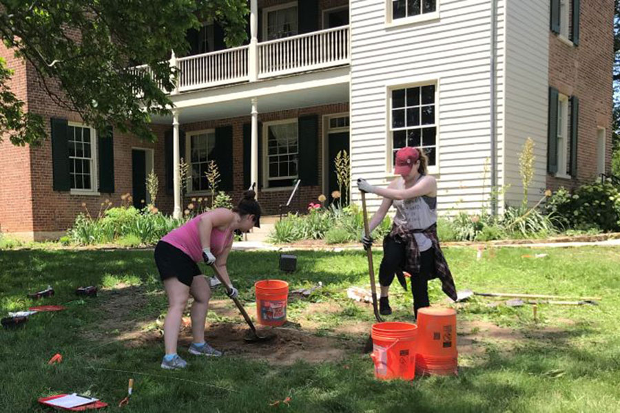 Two students dig in the yard in front of the Wyllie House Museum.