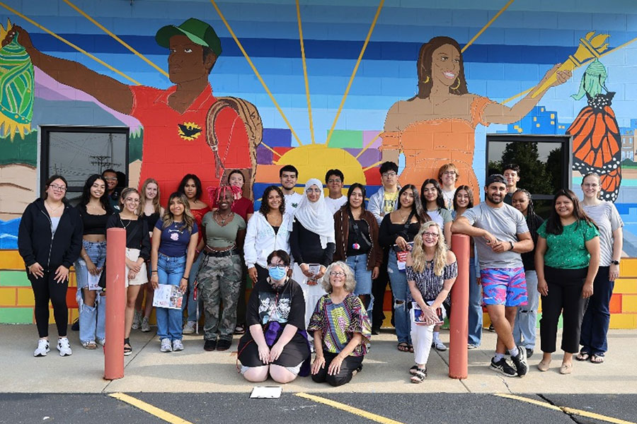 A large group of students stands in front of a mural.