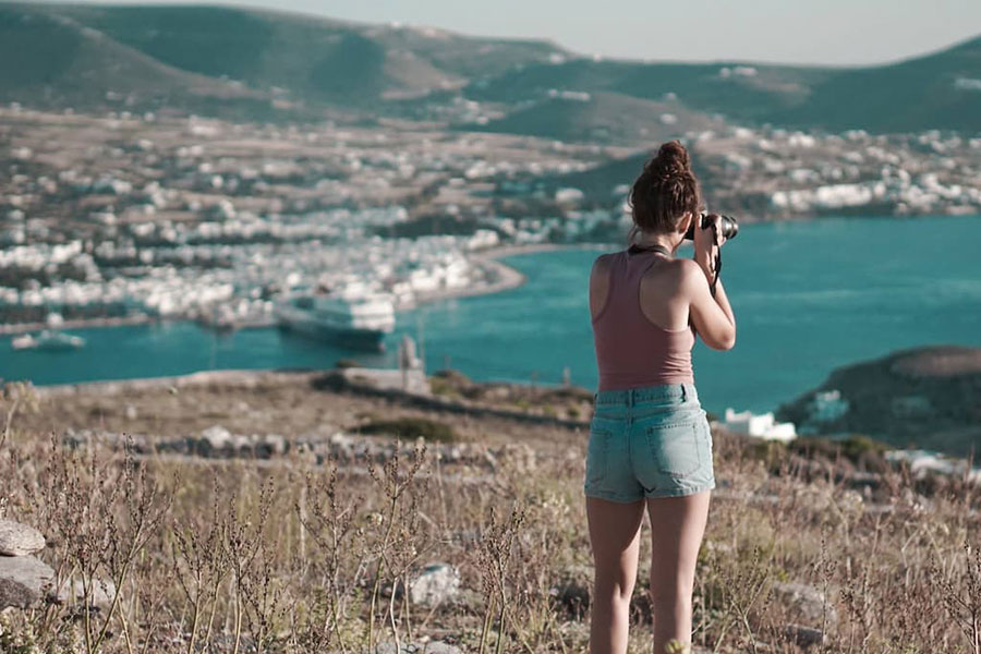 A female student overlooks Greece and takes a picture with a camera.