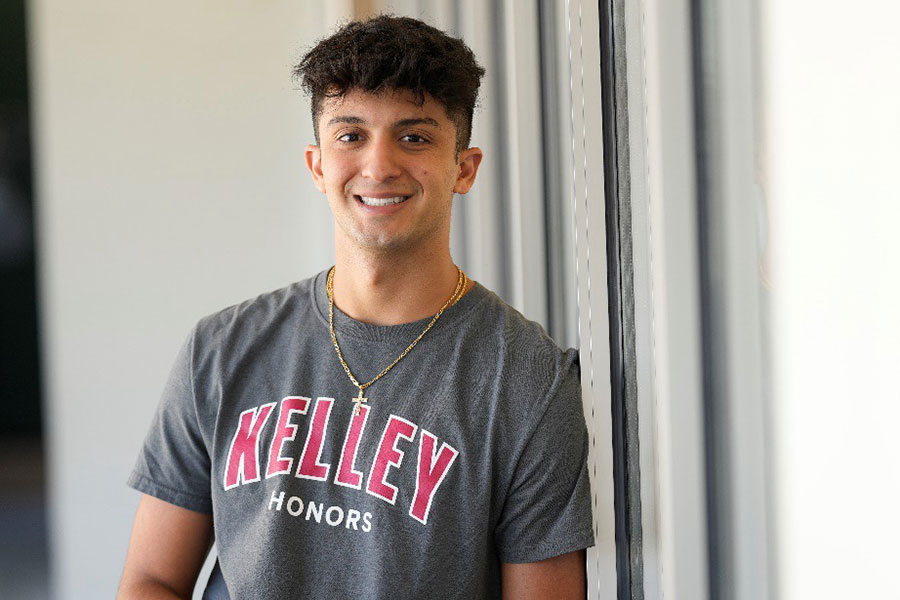 A male student wearing a Kelley Honors shirt stands in a hallway.