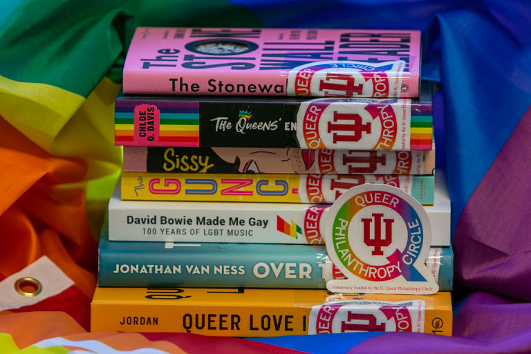 Books on LGBTQ+ stacked on top of a pride flag.