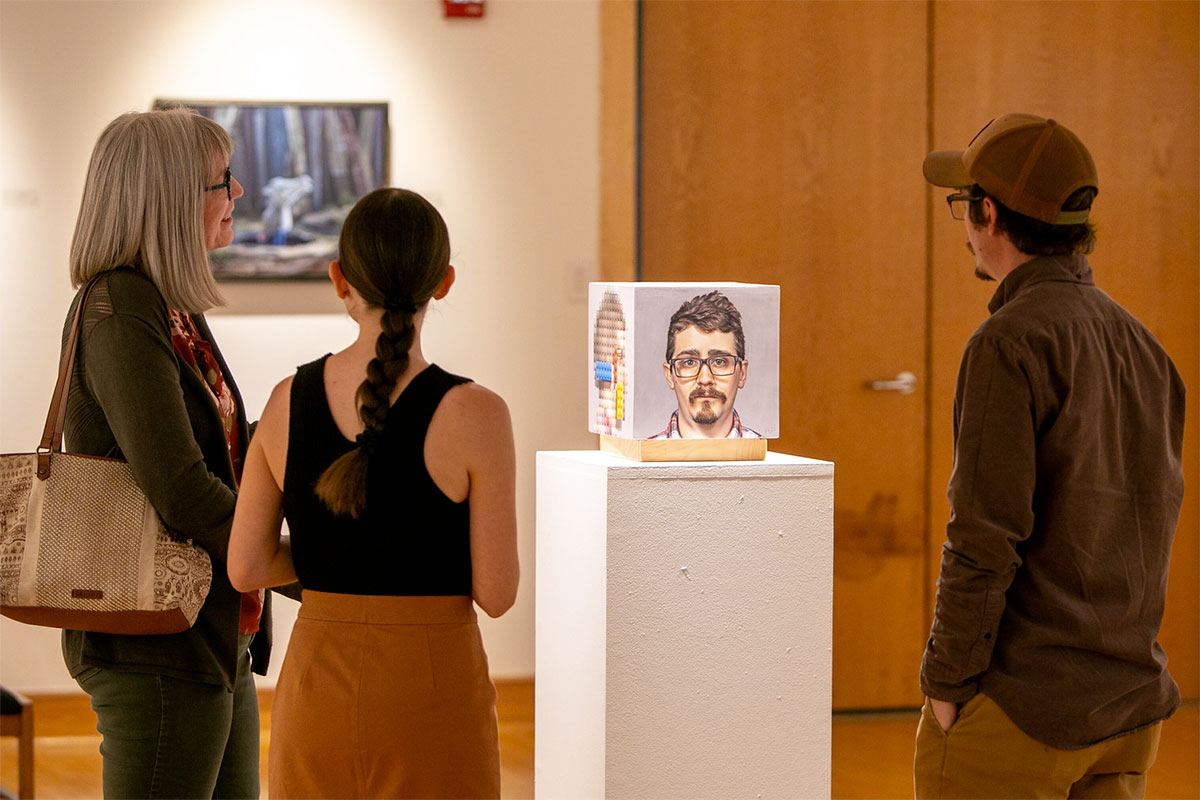 A small group in the art gallery looking on to a three-dimensional portrait displayed on a pedestal.