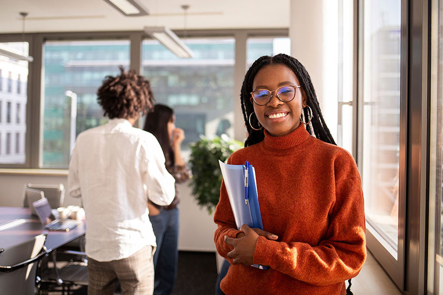 A smiling student holding books stands in a conference room.