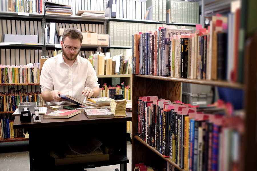 A male student sits at a desk while cataloging books.