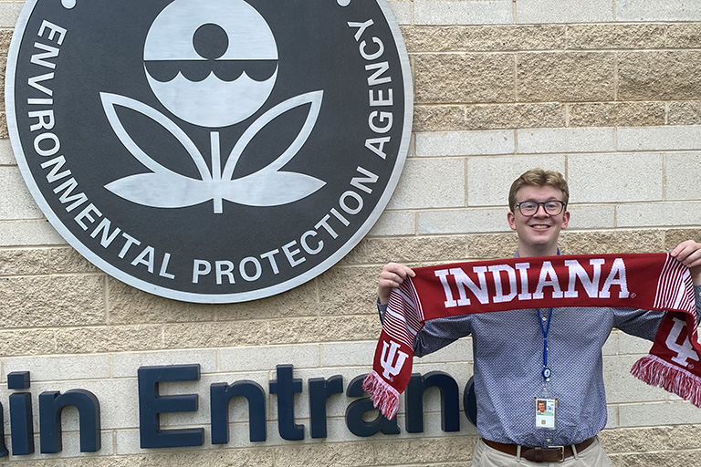 Cooper Sykes stands with an Indiana scarf in front of his internship building at the EPA.