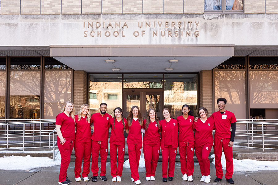 Nursing students in red scrubs posing in front of the Nursing building.