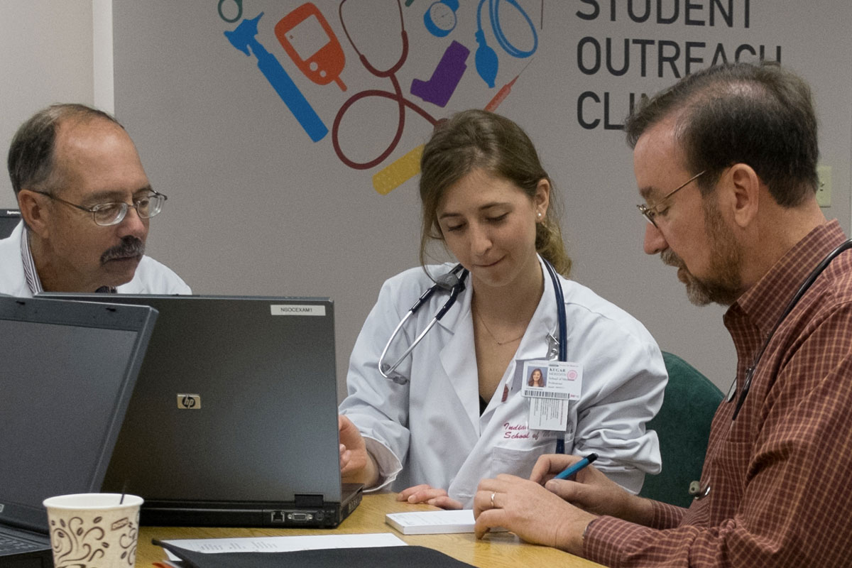 A medical student sitting at a table with laptop computers in between two physicians.