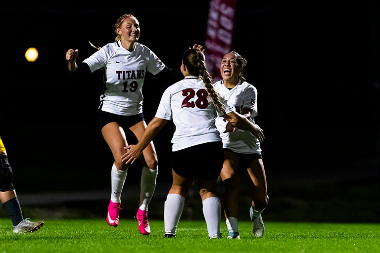 Three female soccer players celebrate on the field.