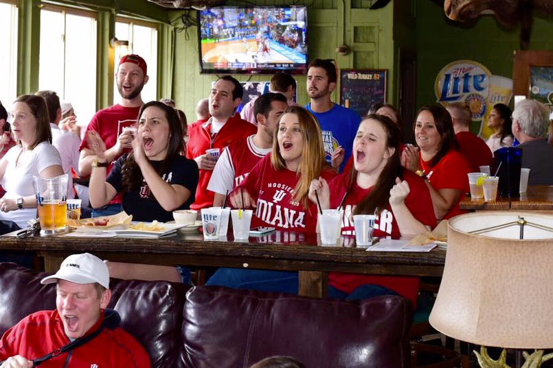 A group of IU alumni cheering while watching a basketball game at a bar.