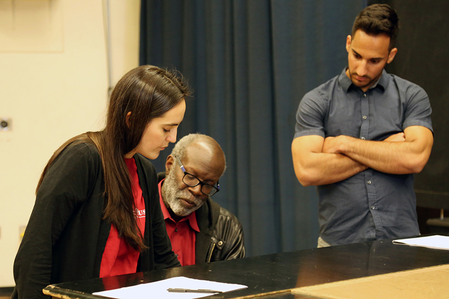 Two students working with a professor at a piano.