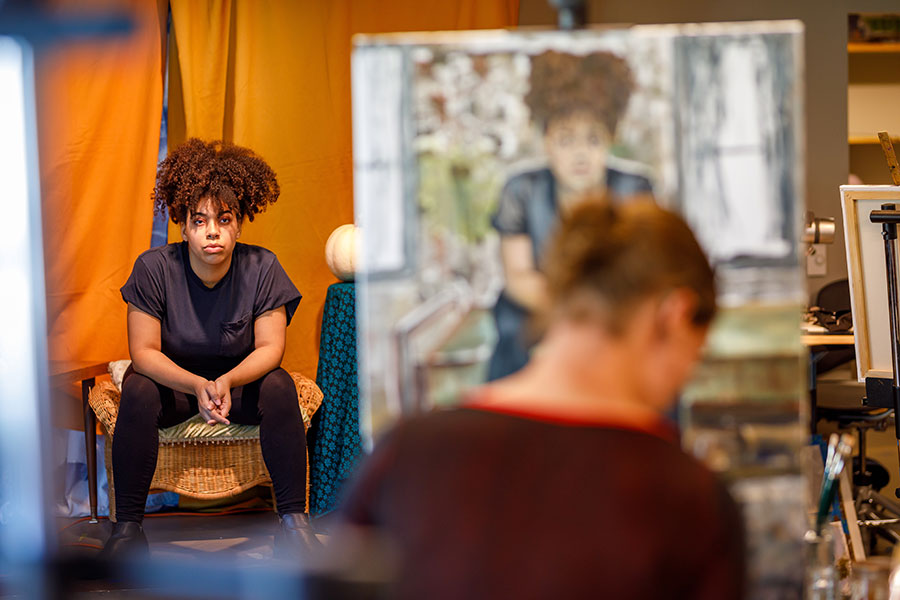 A young woman sits in a chair while her portrait is being painted.